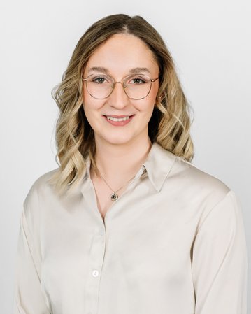 Eine Person mit blonden, lockigen Haaren und Brille trägt ein helles Hemd. Der Hintergrund ist neutral und hell.